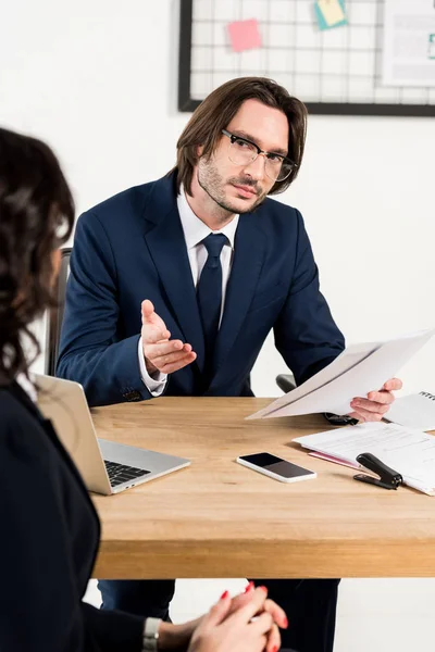 Foyer sélectif du recruteur dans les lunettes à la recherche de femme attrayante et détenant des documents — Photo de stock