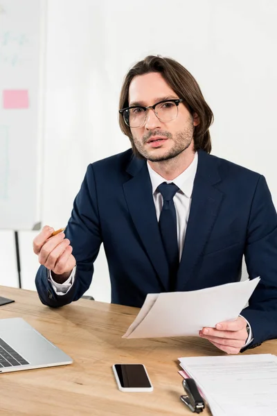 Schöner Mann mit Brille, der Dokumente hält und in die Kamera schaut — Stockfoto