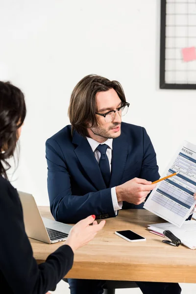 Selective focus of recruiter in glasses looking at resume and gesturing near woman — Stock Photo
