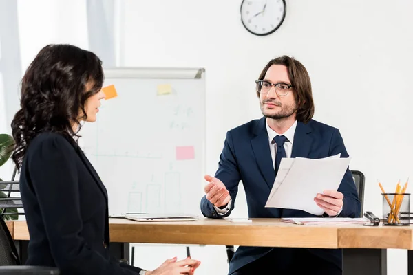 Foco seletivo recrutador bonito em óculos segurando documentos e gestos perto de mulher bonita — Stock Photo