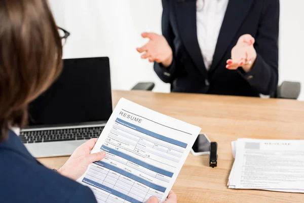 Selective focus of recruiter holding resume near woman gesturing in office — Stock Photo