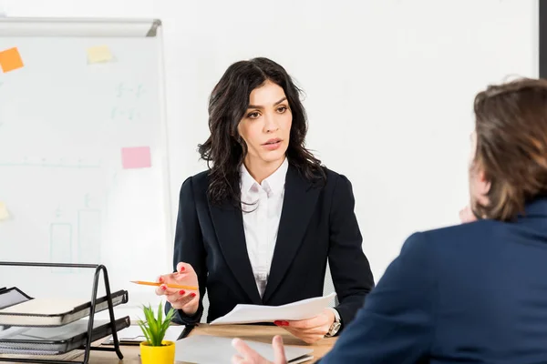 Selektiver Fokus eines attraktiven brünetten Personalvermittlers, der Papier und Bleistift in der Hand hält und den Mann betrachtet — Stockfoto