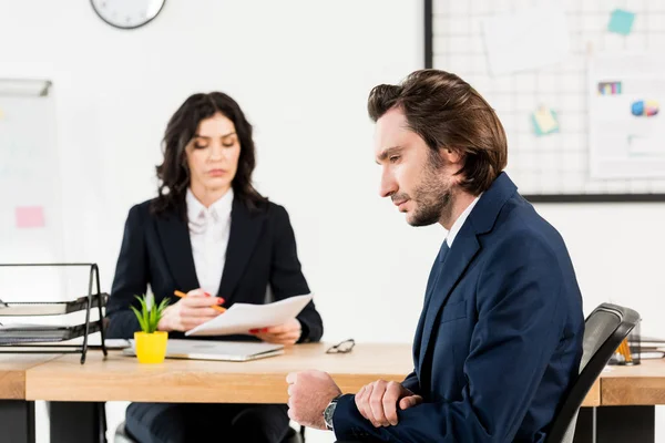Selective focus of handsome man sitting near attractive recruiter in office — Stock Photo
