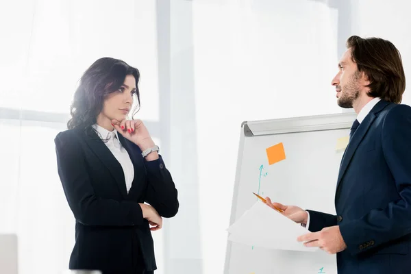 Handsome man holding pencil while standing near white board and looking at pensive woman — Stock Photo