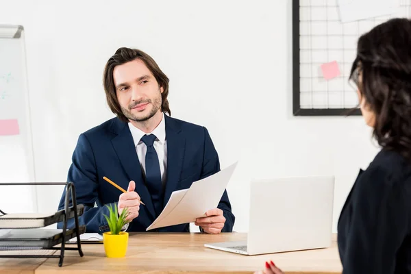 Selective focus of handsome recruiter holding pencil and papers near brunette woman — Stock Photo