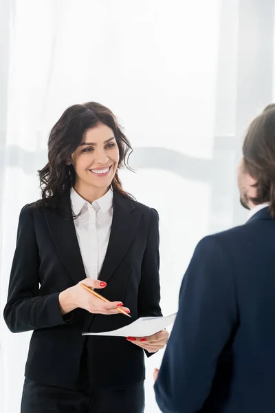 Selective focus of happy woman holding resume and pencil and looking at man — Stock Photo