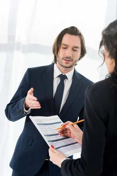 Enfoque selectivo de hombre guapo gesto cerca de la mujer sosteniendo curriculum vitae y lápiz - foto de stock