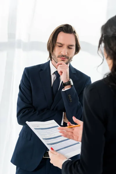 Enfoque selectivo del hombre pensativo de pie cerca de la mujer morena con curriculum vitae en las manos - foto de stock