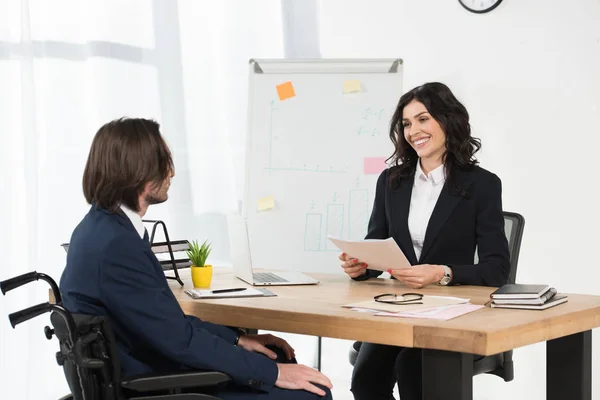 Orologio allegro guardando l'uomo disabile mentre in possesso di documenti e sorridente in ufficio — Foto stock