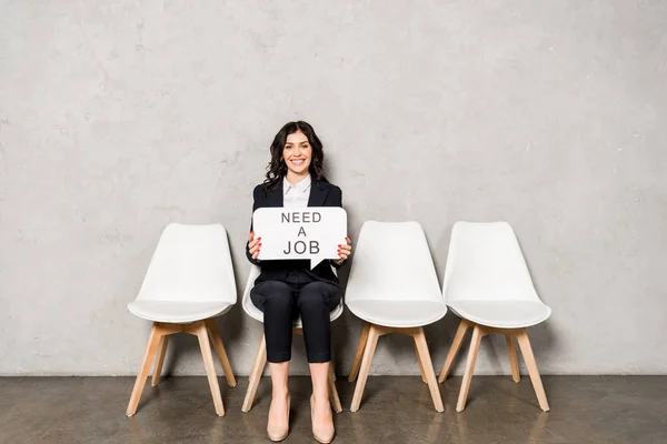 Glückliche brünette Frau mit Sprechblase, die einen Job-Schriftzug braucht, während sie auf dem Stuhl sitzt — Stockfoto