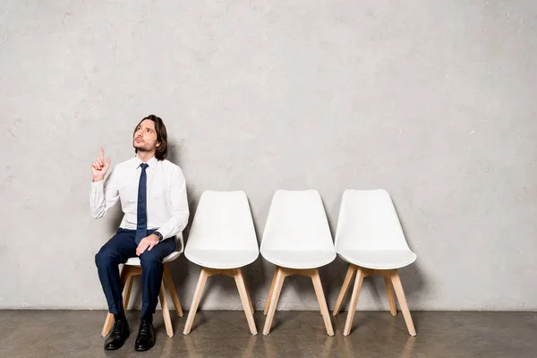 Schöner Mann in formeller Kleidung sitzt auf einem Stuhl und gestikuliert, während er eine Idee hat — Stockfoto