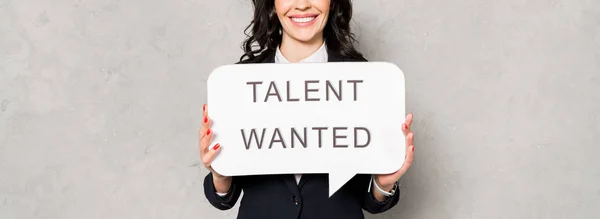 Panoramic shot of happy brunette woman holding speech bubble with talent wanted lettering on grey — Stock Photo