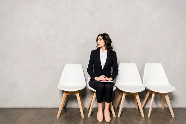 Attractive brunette woman in formal wear sitting on chair with clenched hands — Stock Photo