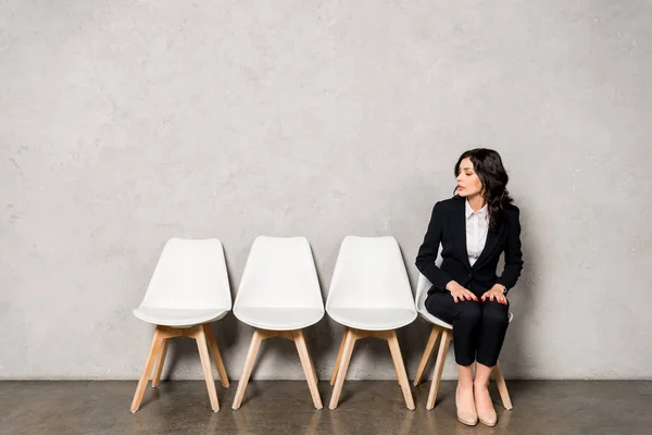 Atractiva morena mujer en formal desgaste sentado en silla antes de entrevista de trabajo - foto de stock