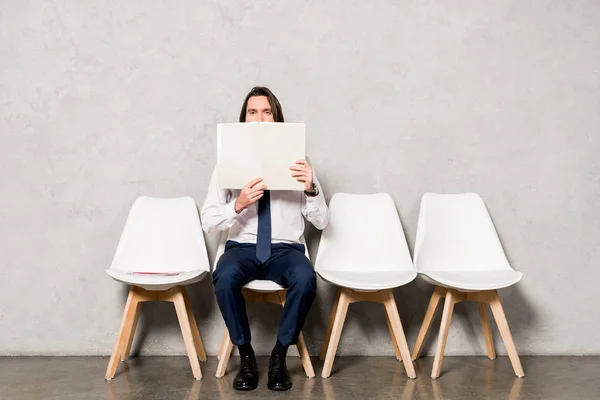 Mann in formeller Kleidung bedeckt Gesicht mit leerem Papier, während er auf Stuhl sitzt — Stockfoto