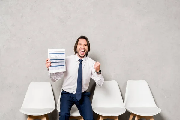 Happy man in formal wear holding resume and gesturing in office — Stock Photo