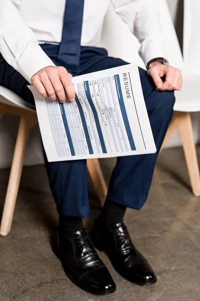 Cropped view of man holding resume while sitting on chair — Stock Photo