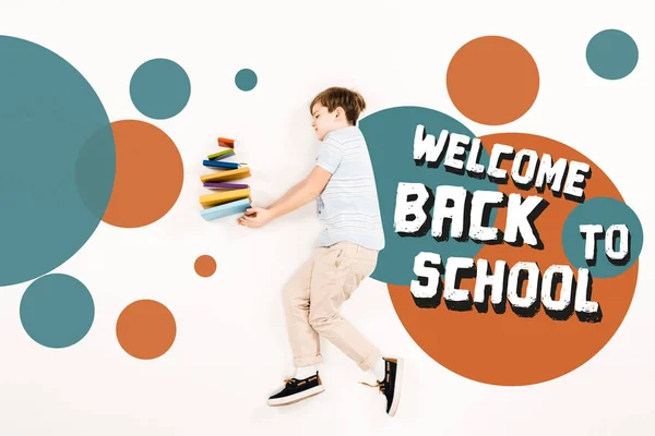 Top view of child near colorful books and welcome back to school lettering on white — Stock Photo