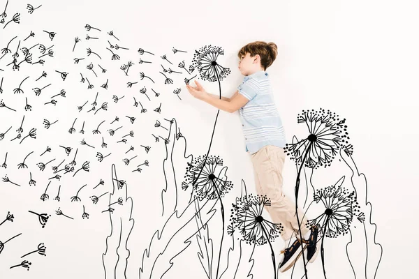 Top view of kid blowing dandelion seeds while flying on white — Stock Photo