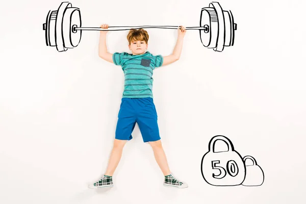 Top view of cute kid holding barbell and looking at camera on white — Stock Photo