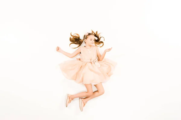 Top view of happy child in pink dress smiling while flying on white — Stock Photo