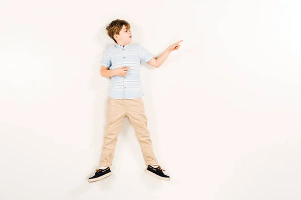 Top view of surprised kid pointing with finger while lying on white — Stock Photo