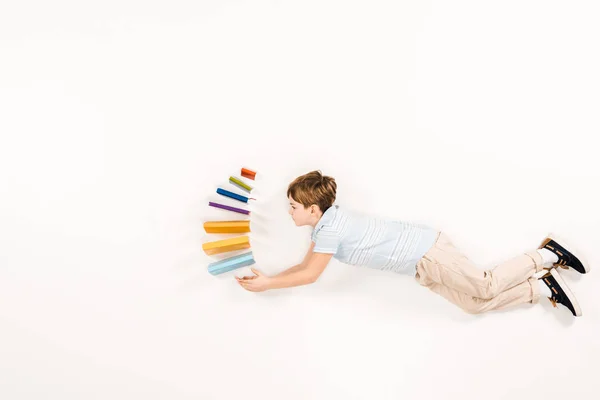 Top view of cute kid holding colorful books while flying on white — Stock Photo