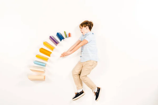 Top view of surprised kid near colorful books on white — Stock Photo