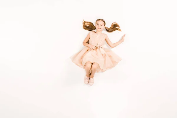 Blick von oben auf ein lächelndes Kind im Kleid, das in die Kamera auf Weiß blickt — Stockfoto
