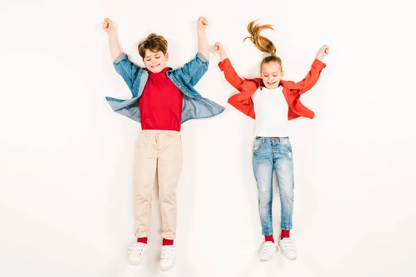Top view of cheerful kids with hands above head lying on white — Stock Photo