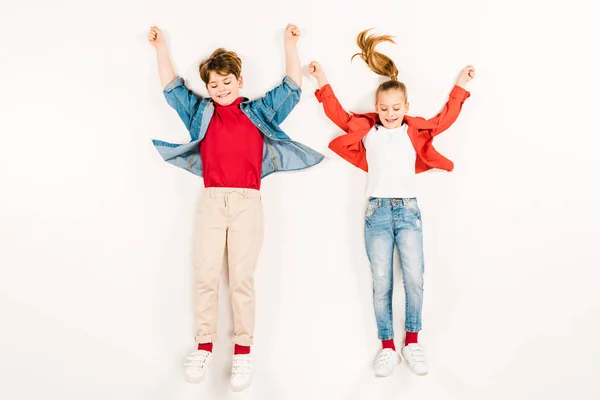 Vue de dessus des enfants joyeux avec les mains au-dessus de la tête couché sur blanc — Photo de stock