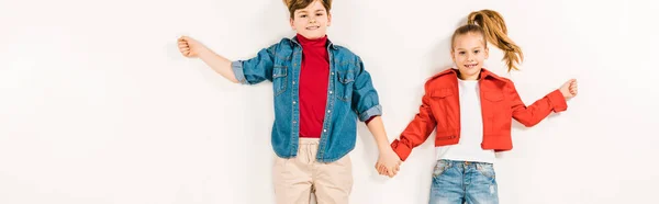 Panoramic shot of cheerful kids holding hands and smiling while lying on white — Stock Photo