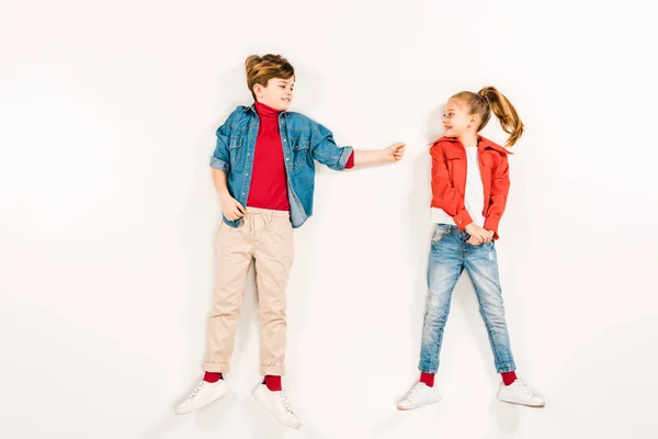 Top view of cheerful kid looking at happy friend while lying on white — Stock Photo