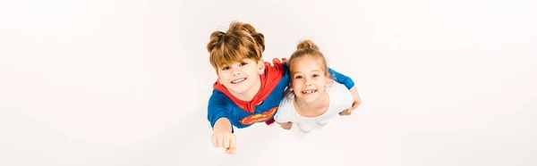 Colpo panoramico di bambino felice in costume da supereroe abbracciando amico e gesticolando sul bianco — Foto stock