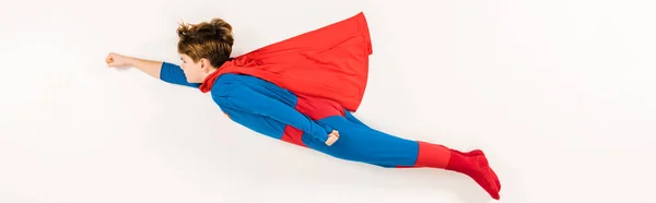 Panoramic shot of adorable kid in super hero costume flying on white — Stock Photo