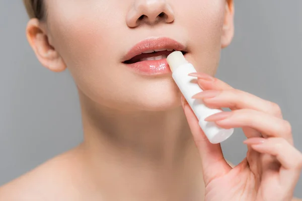Abgeschnittene Ansicht einer jungen Frau mit Lippenbalsam in der Nähe von Lippen isoliert auf grau — Stockfoto