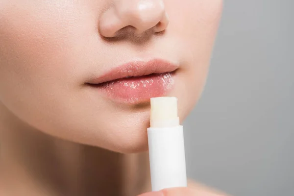 Cropped view of young woman holding lip balm isolated on grey — Stock Photo
