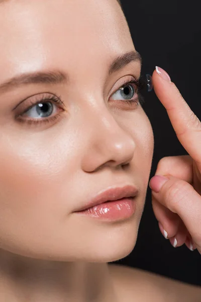 Attractive woman attaching contact lens isolated on black — Stock Photo