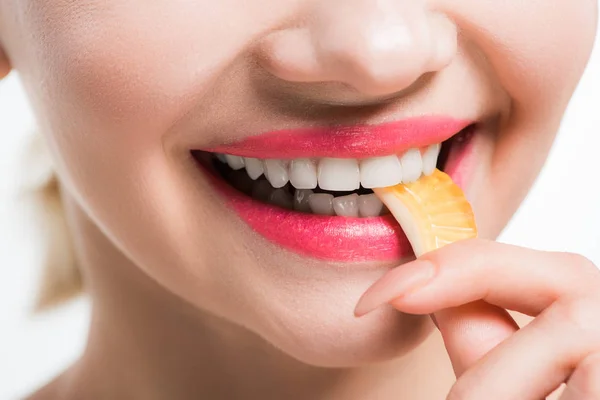 Обрезанный вид улыбающейся женщины, поедающей апельсиновое желе конфеты изолированы на белом — стоковое фото