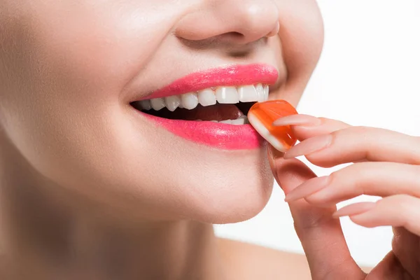 Vue recadrée d'une jeune femme souriante mangeant des bonbons à la gelée d'orange isolés sur blanc — Photo de stock