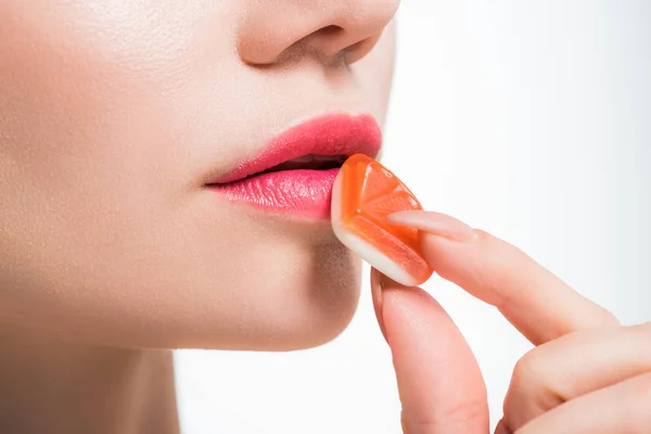 Обрізаний вид жінки, що тримає апельсинові желе-цукерки біля губ на білому — стокове фото