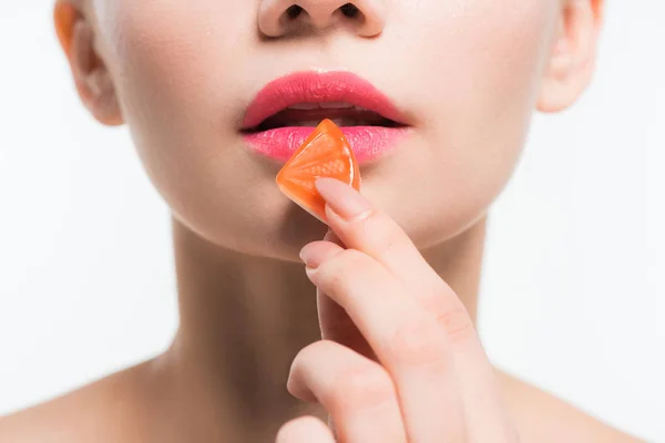 Cropped view of young woman holding orange jelly candy near lips isolated on white — Stock Photo
