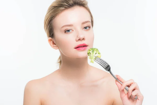 Atractiva mujer desnuda sosteniendo tenedor de plata con brócoli cerca de labios rosados aislados en blanco - foto de stock