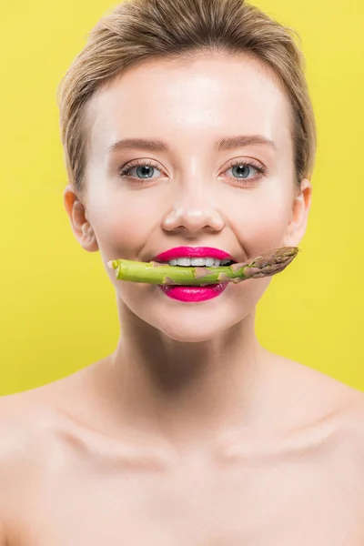 Fröhliche nackte Frau mit grünem und schmackhaftem Spargel im Mund, isoliert auf gelb — Stockfoto