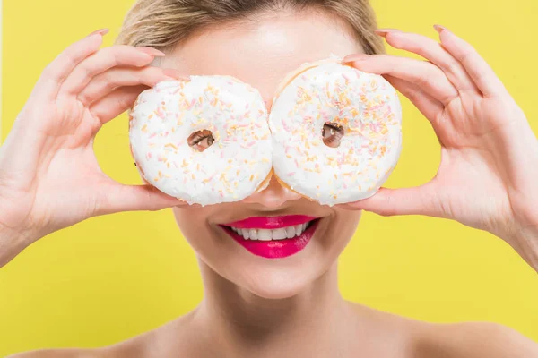 Cheerful woman covering eyes with tasty doughnuts isolated on yellow — Stock Photo
