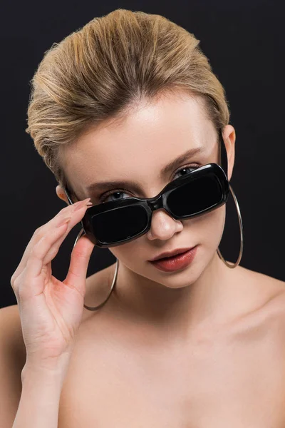 Atractiva joven tocando gafas de sol aisladas en negro - foto de stock