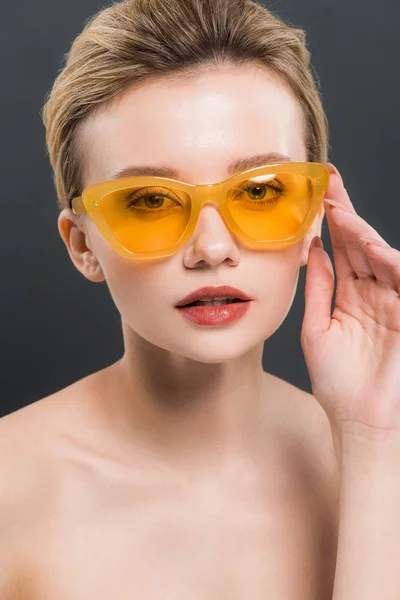 Atractiva joven tocando gafas de sol amarillas aisladas en negro - foto de stock