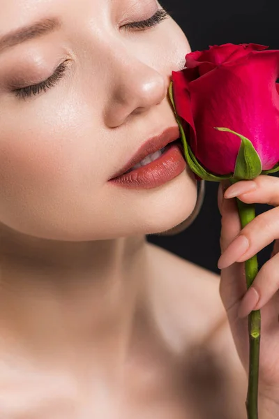 Atractiva joven con los ojos cerrados sosteniendo rosa roja aislada en negro - foto de stock