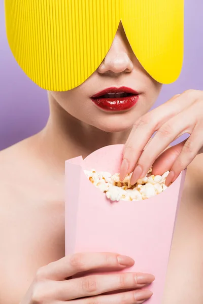 Young woman holding bucket with salty popcorn isolated on purple — Stock Photo