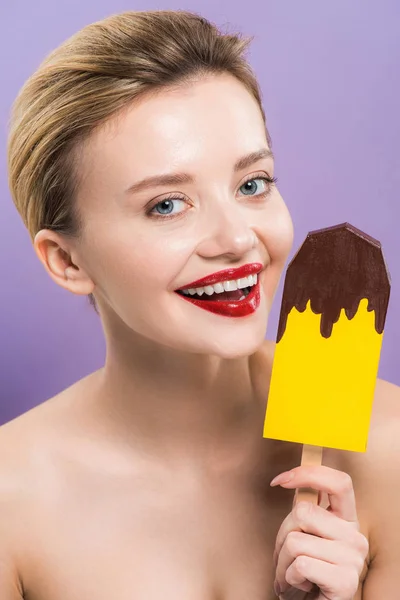 Cheerful woman holding cardboard ice cream and smiling isolated on purple — Stock Photo